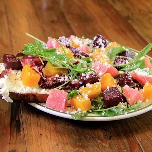 Colorful beet and citrus salad with arugula and cheese on toast, on a wooden table.