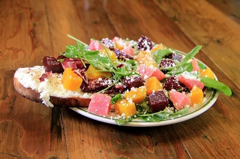 Colorful beet and citrus salad with arugula and cheese on toast, on a wooden table.