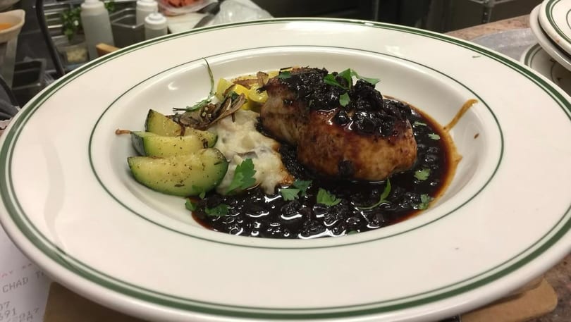 Pork chop with dark berry sauce, mashed potatoes, and zucchini on a white plate.
