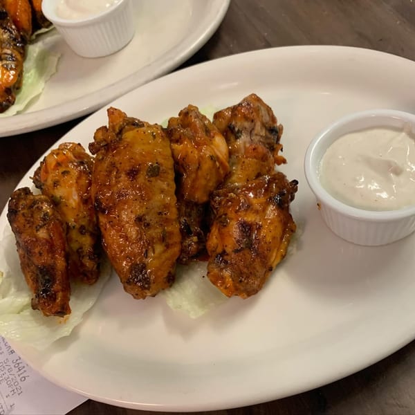A plate of five glazed chicken wings with a side of creamy dipping sauce on lettuce.