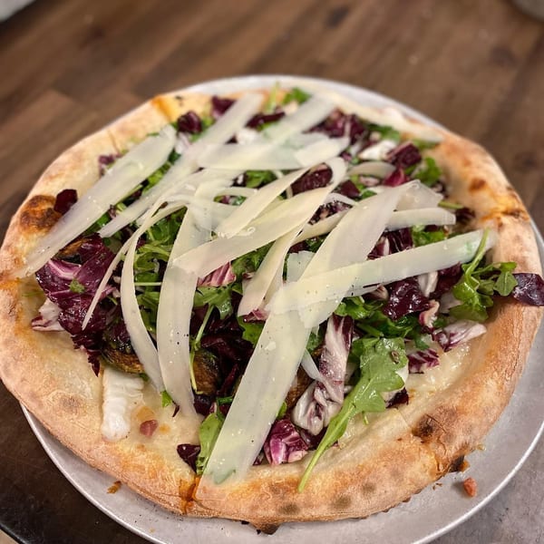A pizza topped with fresh arugula, radicchio, roasted Brussels sprouts, and shaved Parmesan cheese.