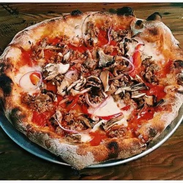 Wood-fired pizza with sausage, mushrooms, red onions, and tomato sauce on a metal tray.