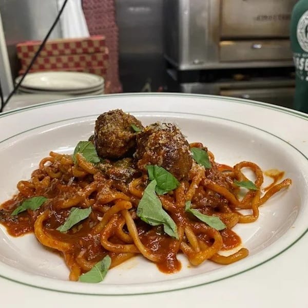 Spaghetti with two large meatballs, red sauce, fresh basil, and grated cheese on a white plate.