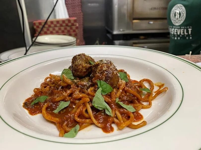 Spaghetti with two large meatballs, red sauce, fresh basil, and grated cheese on a white plate.